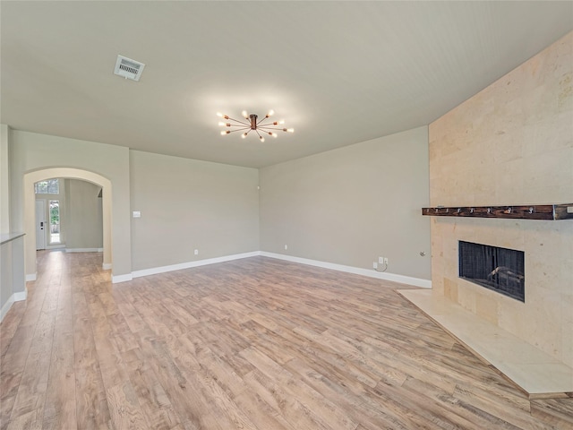 1034 Pelican Dr, Frisco, TX 75033 - unfurnished living room featuring arched walkways, light wood-type flooring, a tiled fireplace, and a chandelier