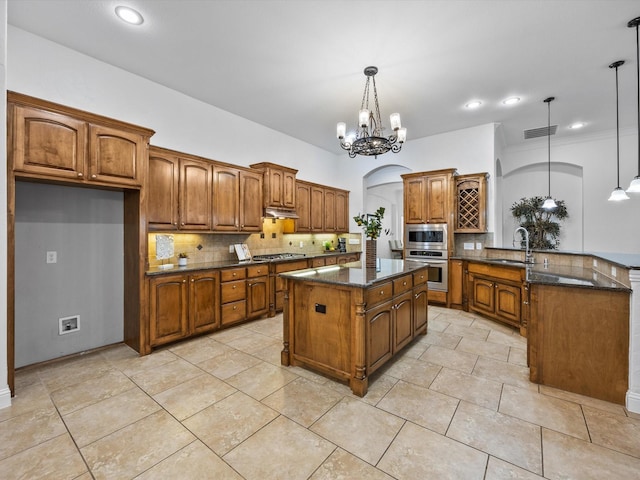 3241 Mindy Ln, Midlothian, TX 76065 - kitchen with stainless steel appliances, brown cabinetry, decorative backsplash, a peninsula, and under cabinet range hood