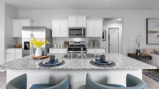 118 Gerber Ln, Boyd, TX 76023 - kitchen featuring appliances with stainless steel finishes, white cabinets, light stone countertops, a kitchen breakfast bar, and a kitchen island with sink