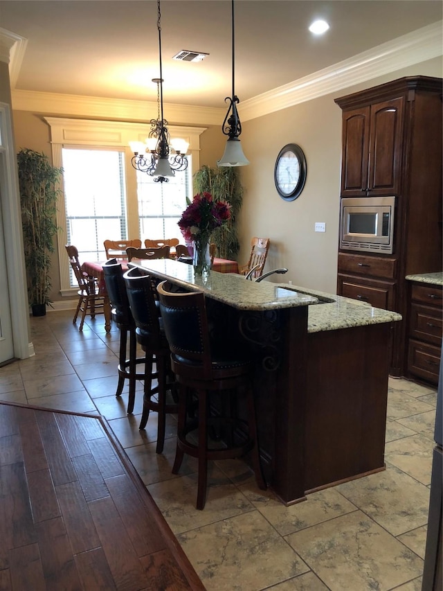 413 Fair Oaks St, Bossier City, LA 71112 - kitchen featuring stainless steel microwave, light stone counters, a breakfast bar, crown molding, and dark brown cabinetry