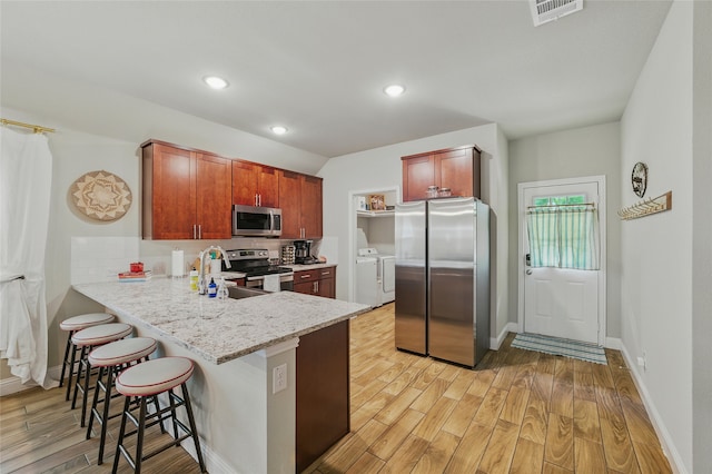 2409 Ross Ave, Fort Worth, TX 76164 - kitchen with stainless steel appliances, washer and clothes dryer, a breakfast bar area, light wood-style floors, and decorative backsplash