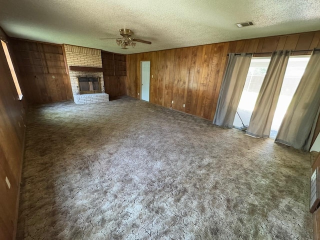 3560 Regal Rd, Fort Worth, TX 76111 - unfurnished living room featuring a ceiling fan, a textured ceiling, wooden walls, carpet flooring, and a brick fireplace