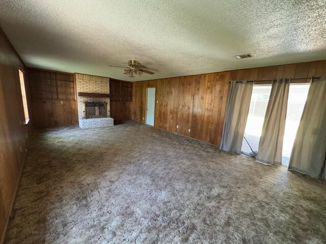 3560 Regal Rd, Fort Worth, TX 76111 - unfurnished living room featuring ceiling fan, a textured ceiling, wood walls, a fireplace, and carpet flooring