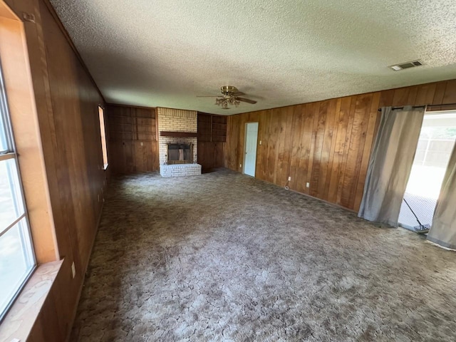 3560 Regal Rd, Fort Worth, TX 76111 - unfurnished living room featuring a textured ceiling, a ceiling fan, wood walls, healthy amount of natural light, and carpet flooring