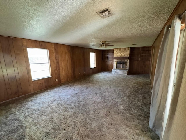 3560 Regal Rd, Fort Worth, TX 76111 - unfurnished living room with a ceiling fan, wood walls, a fireplace, a textured ceiling, and carpet flooring