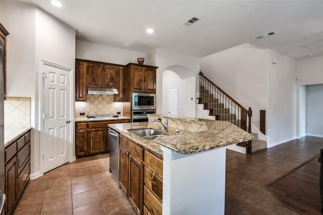 7601 Willowbend Dr, Mckinney, TX 75071 - kitchen with appliances with stainless steel finishes, arched walkways, tasteful backsplash, an island with sink, and dark tile patterned flooring