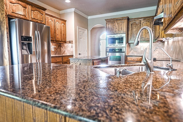 104 Coldwater Creek Ln, Weatherford, TX 76088 - kitchen with appliances with stainless steel finishes, arched walkways, decorative backsplash, brown cabinets, and crown molding