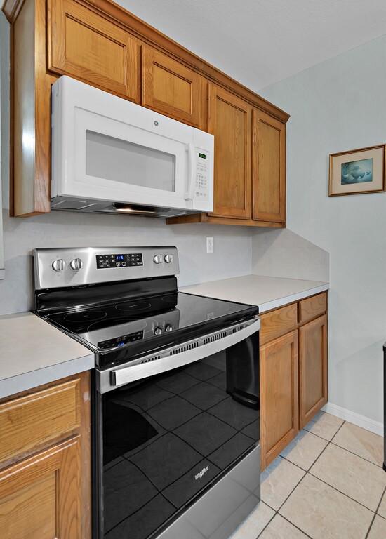 308 Greystone Dr, Lorena, TX 76655 - kitchen with stainless steel range with electric cooktop, white microwave, light tile patterned flooring, brown cabinets, and light countertops