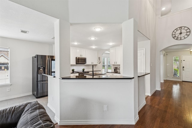 2708 Ferdinand, Grand Prairie, TX 75054 - kitchen featuring appliances with stainless steel finishes, arched walkways, dark countertops, white cabinets, and wood finished floors