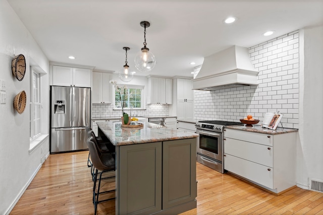 7845 Blackbird Ln, Dallas, TX 75238 - kitchen featuring stainless steel appliances, premium range hood, white cabinets, decorative backsplash, and a kitchen bar