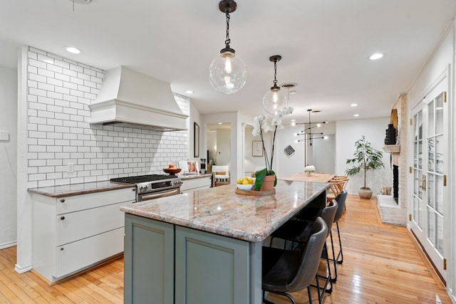 7845 Blackbird Ln, Dallas, TX 75238 - kitchen featuring custom range hood, stainless steel gas stove, backsplash, light wood-type flooring, and a kitchen island