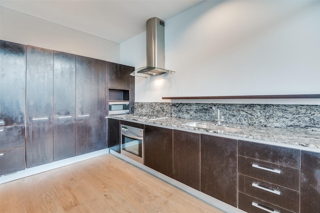 2430 Victory Park Ln Unit 1906, Dallas, TX 75219 - kitchen with appliances with stainless steel finishes, island range hood, light wood-style floors, light stone counters, and dark brown cabinetry