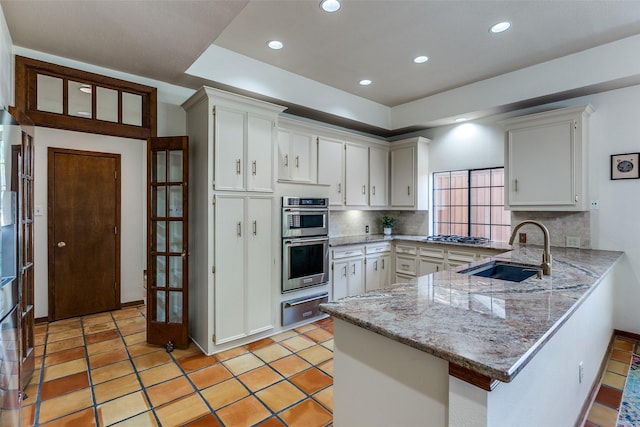 1507 Abrams Rd, Dallas, TX 75214 - kitchen featuring a warming drawer, a peninsula, decorative backsplash, stainless steel appliances, and white cabinetry