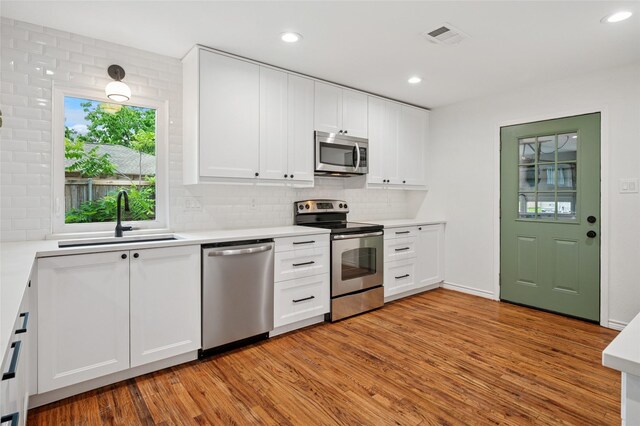 522 Carol Ct, Richardson, TX 75081 - kitchen with appliances with stainless steel finishes, light wood-style flooring, decorative backsplash, white cabinetry, and recessed lighting
