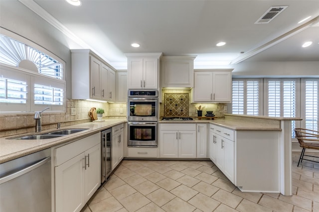 6404 Camille Ave, Dallas, TX 75252 - kitchen featuring appliances with stainless steel finishes, a peninsula, beverage cooler, light countertops, and ornamental molding