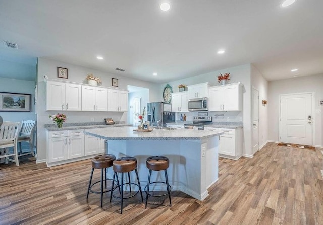 421 Atmore St, Azle, TX 76020 - kitchen with appliances with stainless steel finishes, a breakfast bar area, white cabinetry, light wood-style flooring, and recessed lighting