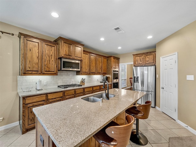 7804 Rocky Mountain Ln, Mckinney, TX 75070 - kitchen with appliances with stainless steel finishes, brown cabinetry, a kitchen breakfast bar, a kitchen island with sink, and tasteful backsplash