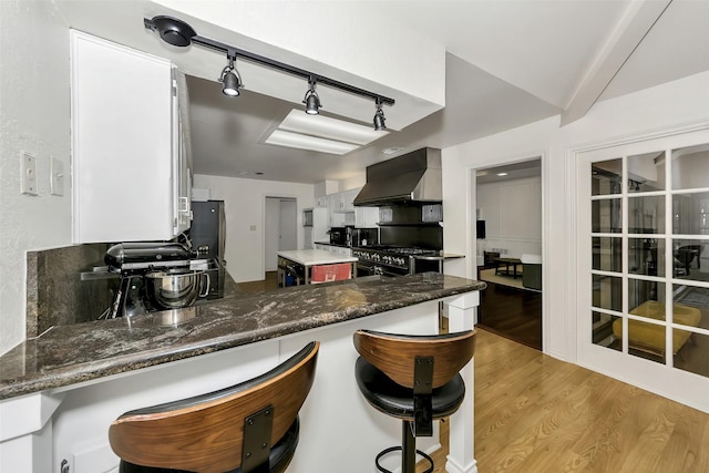 2425 Northgate Dr W, Irving, TX 75062 - kitchen with wall chimney exhaust hood, appliances with stainless steel finishes, light wood finished floors, white cabinets, and a peninsula
