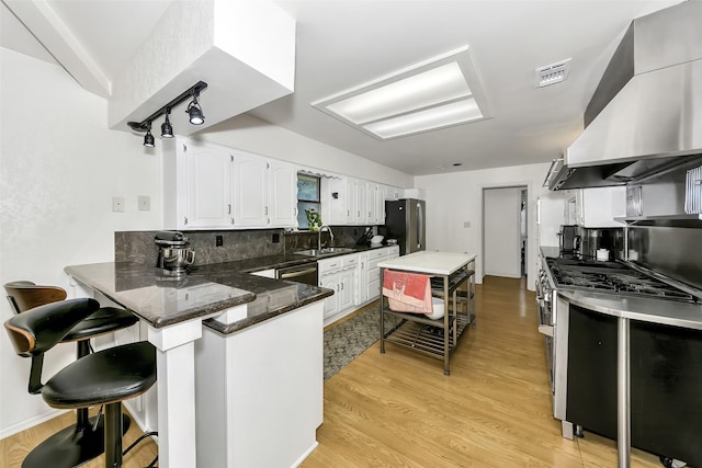 2425 Northgate Dr W, Irving, TX 75062 - kitchen with appliances with stainless steel finishes, wall chimney exhaust hood, white cabinets, a peninsula, and a kitchen breakfast bar