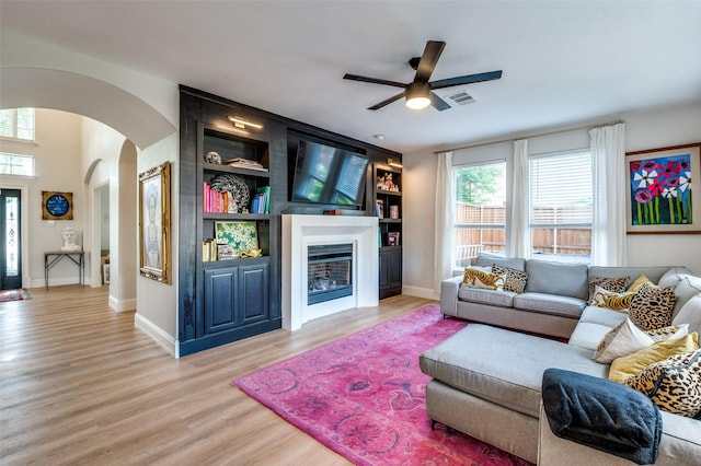 1404 Settlers Ct, Allen, TX 75002 - living room featuring arched walkways, a ceiling fan, light wood-style flooring, built in shelves, and a glass covered fireplace
