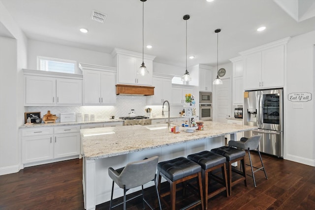 1208 S Pecan Pkwy, Northlake, TX 76247 - kitchen featuring appliances with stainless steel finishes, backsplash, dark wood-style flooring, white cabinetry, and a center island with sink