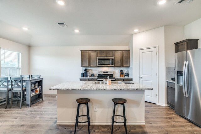 706 Meadow Creek Ln, Josephine, TX 75189 - kitchen featuring appliances with stainless steel finishes, a center island with sink, dark brown cabinetry, dark wood-type flooring, and light stone counters