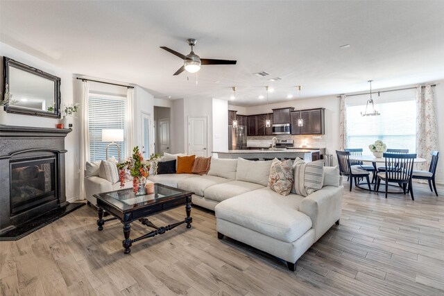 604 Grand Falls Ln, Mckinney, TX 75071 - living area featuring a glass covered fireplace, a ceiling fan, light wood-style flooring, and a chandelier