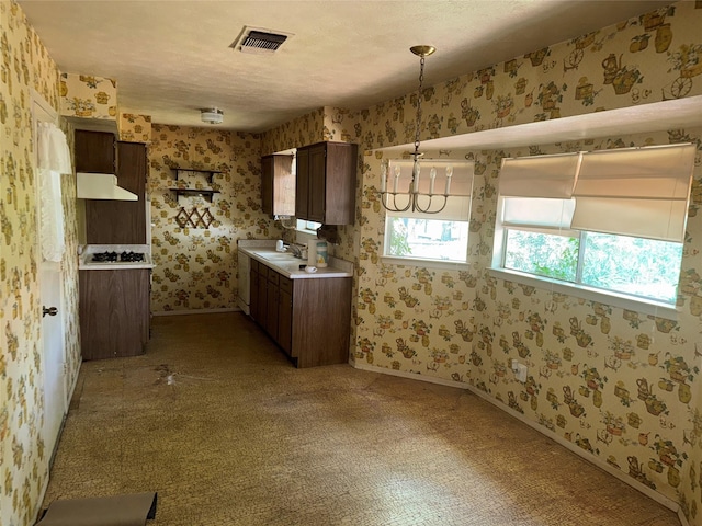 1815 Redwood St, Arlington, TX 76014 - kitchen with under cabinet range hood, wallpapered walls, gas cooktop, light countertops, and dark brown cabinets