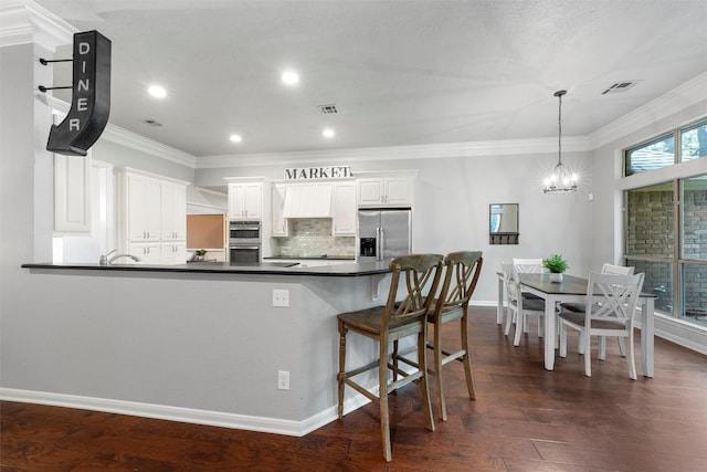 9604 Oak Springs Dr, Woodway, TX 76712 - kitchen featuring appliances with stainless steel finishes, dark countertops, a chandelier, ornamental molding, and a peninsula