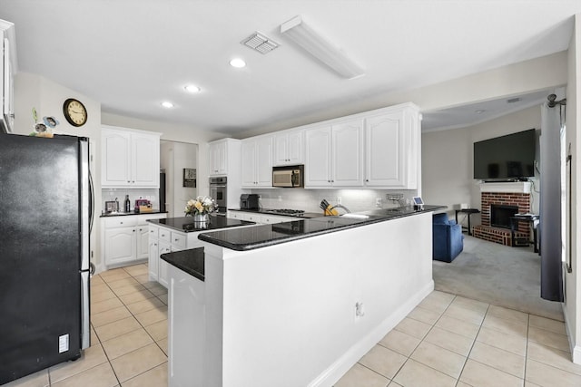 13272 Blue Jean Dr, Fort Worth, TX 76052 - kitchen featuring appliances with stainless steel finishes, light tile patterned floors, dark countertops, a fireplace, and white cabinets