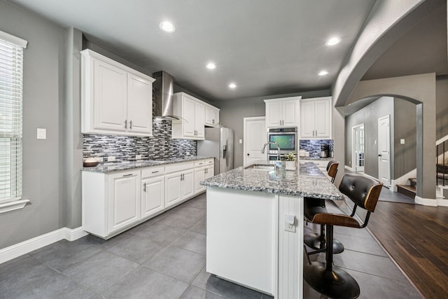 1017 Appalachian Ln, Savannah, TX 76227 - kitchen featuring appliances with stainless steel finishes, wall chimney range hood, decorative backsplash, a breakfast bar area, and arched walkways