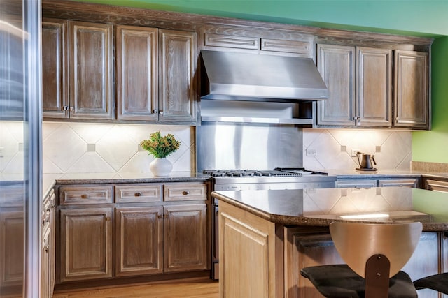 3505 Turtle Creek Blvd Unit 2A, Dallas, TX 75219 - kitchen with under cabinet range hood, a breakfast bar, decorative backsplash, and dark stone counters