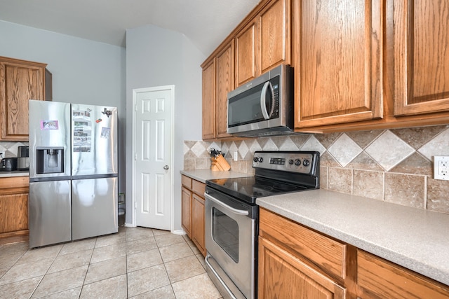703 Monterey Dr, Rockwall, TX 75087 - kitchen with appliances with stainless steel finishes, brown cabinetry, light tile patterned floors, tasteful backsplash, and vaulted ceiling