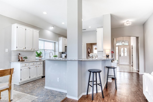 400 Patricia Ln, Highland Village, TX 75077 - kitchen featuring a breakfast bar area, a peninsula, white cabinetry, light stone countertops, and tasteful backsplash