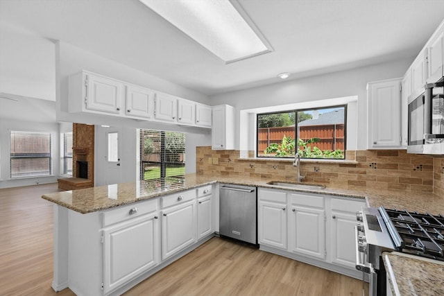 1800 Chatham Dr, Flower Mound, TX 75028 - kitchen featuring appliances with stainless steel finishes, a peninsula, a brick fireplace, and light wood-style floors