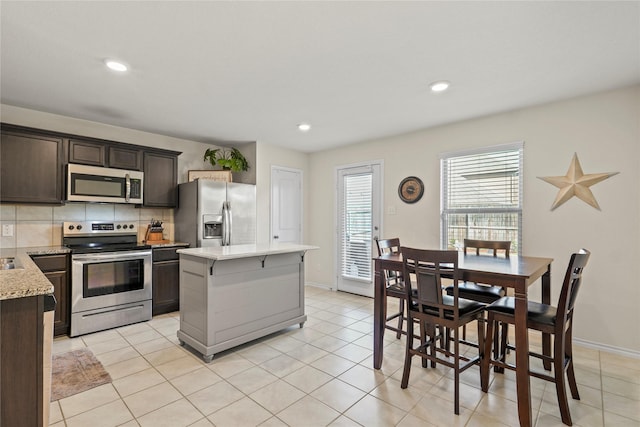 2300 Torch Lake Dr, Forney, TX 75126 - kitchen with appliances with stainless steel finishes, dark brown cabinetry, backsplash, a kitchen island, and light tile patterned floors