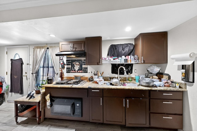 3832 Mount Ranier St, Dallas, TX 75211 - kitchen featuring stainless steel gas stovetop, black microwave, under cabinet range hood, dark brown cabinets, and light countertops