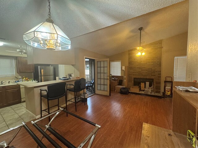 1909 Cloisters Dr Unit 1025, Arlington, TX 76011 - dining area with a ceiling fan, vaulted ceiling, a textured ceiling, light wood-type flooring, and a brick fireplace