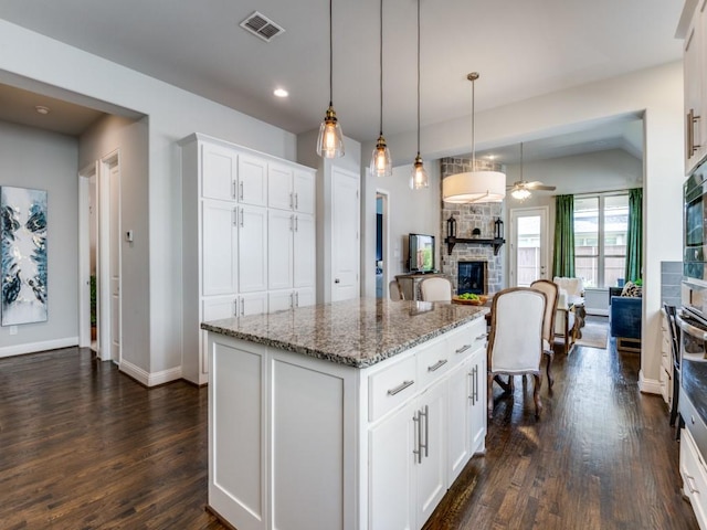 4141 Maclin Dr, Celina, TX 75009 - kitchen featuring a stone fireplace, dark wood-style floors, light stone counters, white cabinetry, and a kitchen island