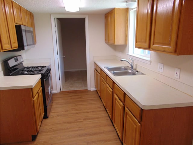 6207 Misty Wood Dr, Dallas, TX 75217 - kitchen with appliances with stainless steel finishes, light wood finished floors, light countertops, brown cabinetry, and a textured ceiling