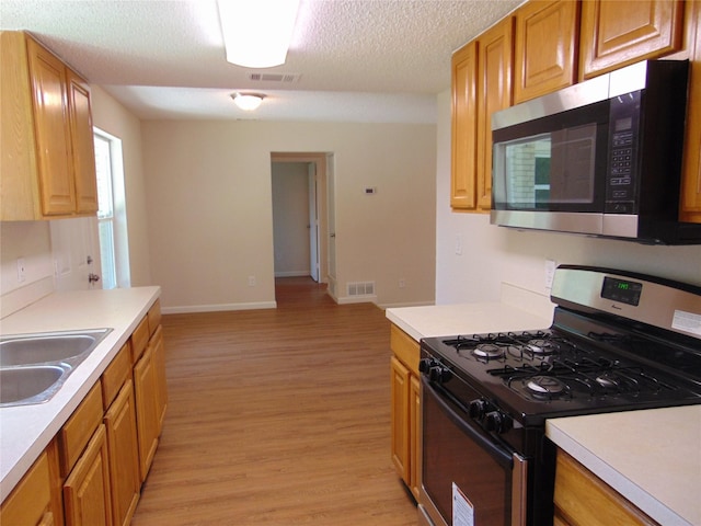 6207 Misty Wood Dr, Dallas, TX 75217 - kitchen with appliances with stainless steel finishes, light countertops, light wood-style flooring, and a textured ceiling