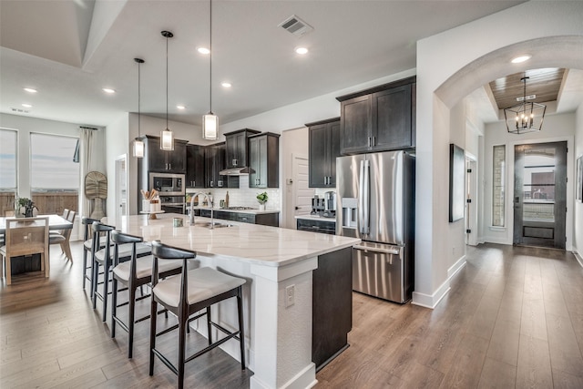 1887 Silver Birch Rd, Waxahachie, TX 75165 - kitchen with stainless steel appliances, arched walkways, light stone countertops, wood finished floors, and a breakfast bar area