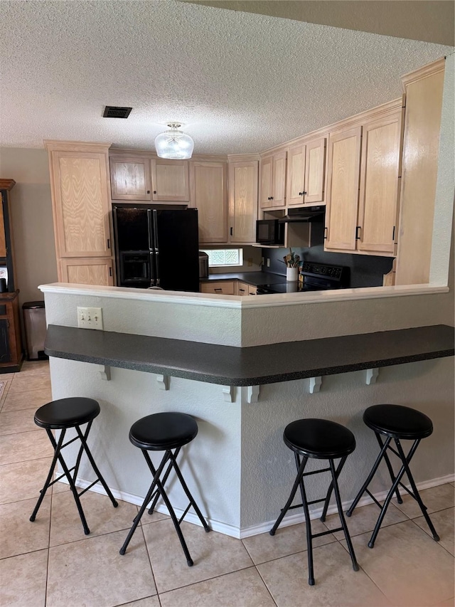 907 Dogwood St, Waco, TX 76706 - kitchen with black appliances, a peninsula, light brown cabinets, dark countertops, and a textured ceiling