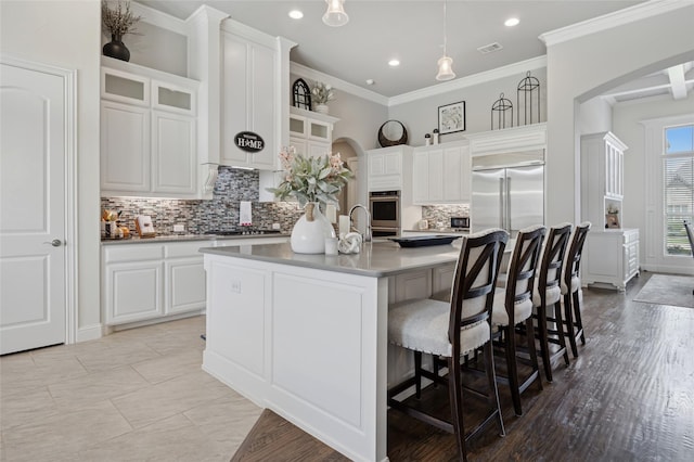 4513 Donnoli Dr, Flower Mound, TX 75022 - kitchen with arched walkways, decorative backsplash, stainless steel appliances, a center island with sink, and white cabinets