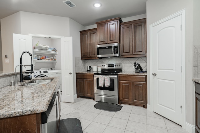680 Navasota Dr, Crandall, TX 75114 - kitchen featuring appliances with stainless steel finishes, washer and clothes dryer, light tile patterned floors, backsplash, and light stone counters