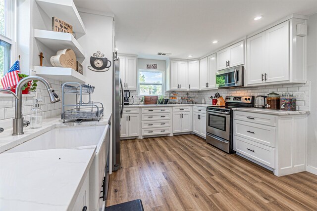 3135 Brazos River Dr, Granbury, TX 76048 - kitchen with stainless steel appliances, open shelves, light wood-type flooring, backsplash, and white cabinets