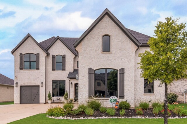 3900 Brazoria Dr, Prosper, TX 75078 - french country style house with concrete driveway, an attached garage, brick siding, and roof with shingles