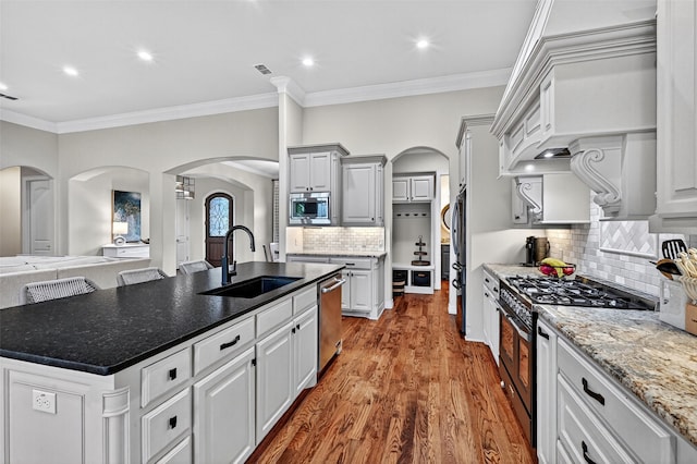 2427 Remuda Dr, Sherman, TX 75092 - kitchen with appliances with stainless steel finishes, arched walkways, a center island with sink, wood finished floors, and ornamental molding
