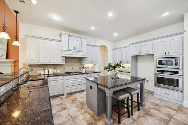 6873 Martel Pl, Frisco, TX 75035 - kitchen with appliances with stainless steel finishes, arched walkways, dark stone countertops, a breakfast bar, and decorative backsplash