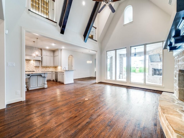 2911 Blackthorn Dr, Prosper, TX 75078 - unfurnished living room with a ceiling fan, high vaulted ceiling, dark wood-type flooring, a stone fireplace, and beamed ceiling